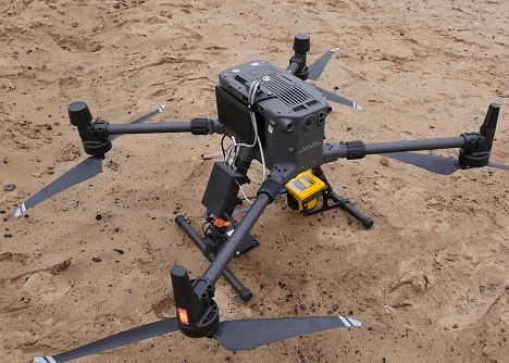 Multi-rotor drone fitted with a methane detection sensor, positioned on the ground.