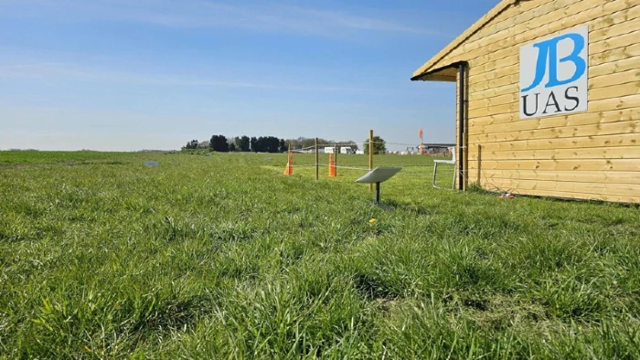 SkyHut at Test and Trial Centre A grassy field under a blue sky, next to a wooden building with a sign that reads "JBUAS".