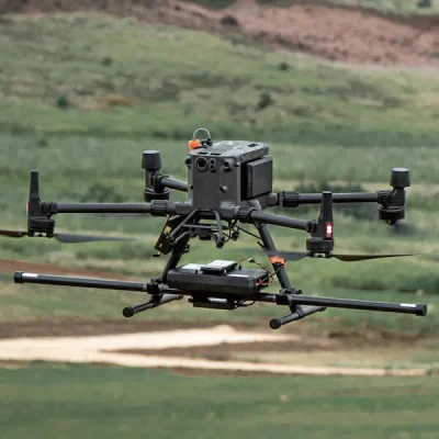 A multi-rotor drone carrying a SENSYS MagDrone R3 magnetometer payload flying over open countryside during a geophysical surveying operation.