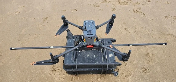 NRP Redcar SENSYS R4 581x272 Survey drone with a geophysical sensor payload positioned on a protective equipment case on a beach.